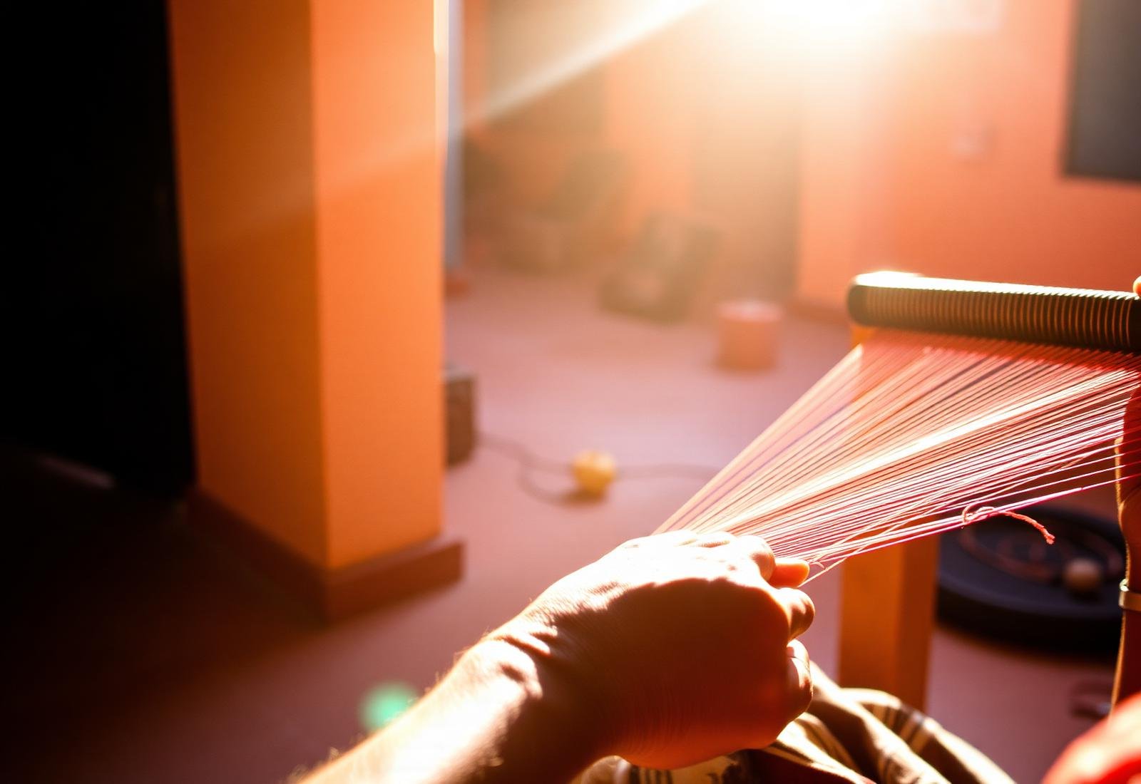 Hands of a rural artisan weaving colourful yarn on a small handloom in warm sunlight